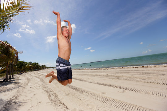 Stock image of a senior man jumping on the beach