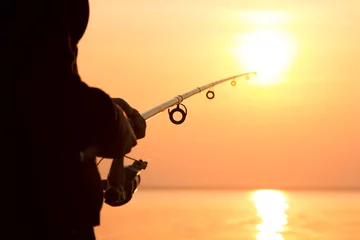 Acrylic prints Fishing young girl fishing at sunset near the sea