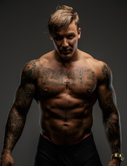 Fototapeta na wymiar Tattooed muscular guy posing on gray background