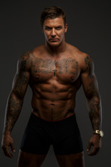 Fototapeta na wymiar Tattooed muscular guy posing on gray background