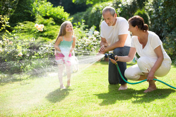 Mädchen, Vater und Oma spielen mit Gartenschlauch