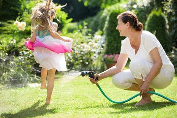 Mädchen springt über Spritzwasser aus Gartenschlauch