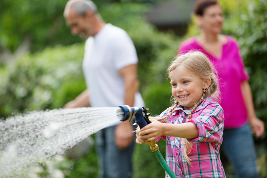 M&auml;dchen mit Gartenschlauch hat Spa&szlig; im Garten