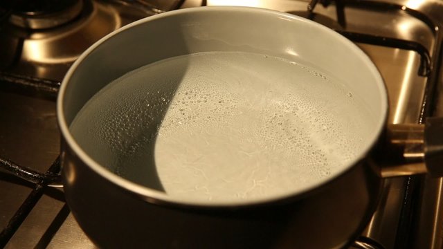 A view of a pot on an oven with water starting to boil