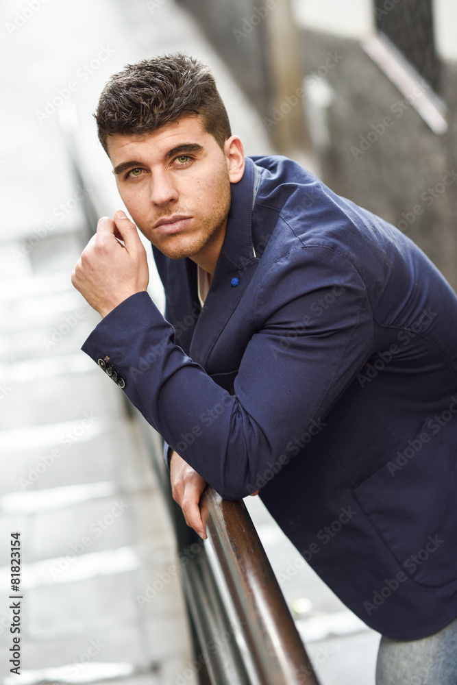 Wall mural Handsome young man with blue eyes posing near a wall