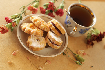 Jam cookies on the plate, a cup of tea and dried carnations
