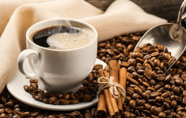 Close-up of coffee cup with roasted coffee beans on wooden background.