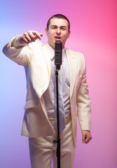 Man in white suit  with microphone. Vivid emotions. Colored back