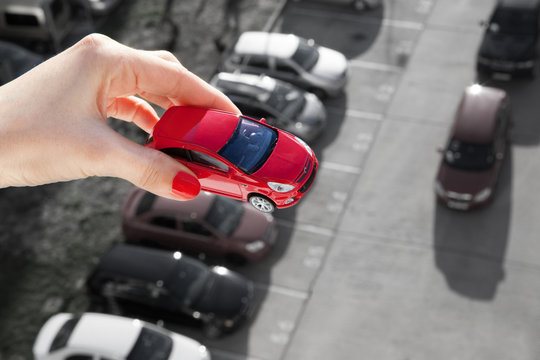 Dream to have a car. Hand holding a red toy car over parking.