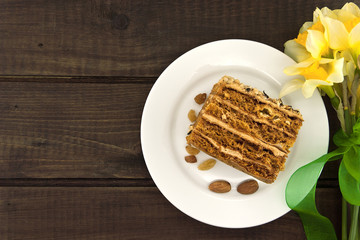 Cake slice with nut on plate on wooden table. Bouquet of flowers