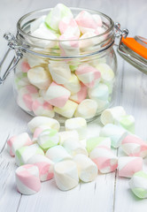 Colorful marshmallows in glass jar on light wooden background