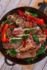 Frying pan with fried meat, bacon, red pepper and spinach