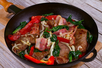 Frying pan with fried meat, bacon, red pepper and spinach