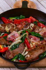 Frying pan with fried meat, bacon, red pepper and spinach