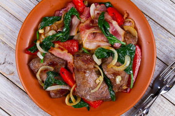 Fried meat, bacon, red paprika pepper and spinach plate