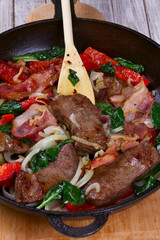 Frying pan with fried meat, bacon, red pepper and spinach