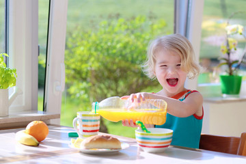 Happy toddler girl enjoying healthy breakfast in sunny kitchen