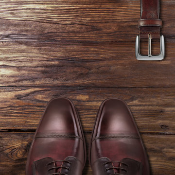 Classic male brown leather shoes with belt on wood