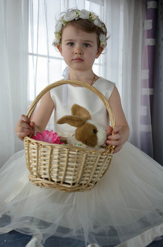 Маленькая девочка в белом платье с кроликом в корзинке