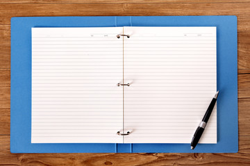Student's desk with open book or blue project folder with ballpoint pen ready for writing homework...