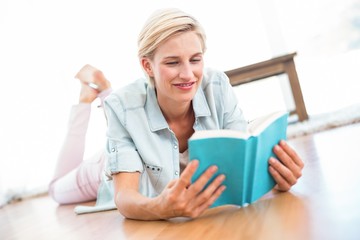 Pretty blonde woman lying on the floor and reading a book