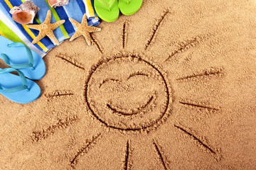 Beach with smiling face sun drawn drawing in sand with summer holiday vacation accessories towel...
