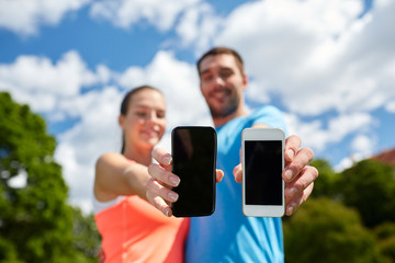 two smiling people with smartphones outdoors