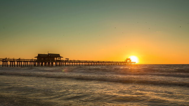 Sunset over horizon and wooden pier of caribbean beach of Naples in Florida. Panning and zoom in Time Lapse.