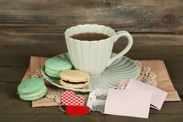 Heart shaped teabag tags, macaroons and cup of tea on wooden background