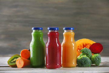 Glass bottles of fresh healthy juice with set of fruits and vegetables on wooden background
