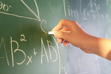 Teacher hand writing formulas on blackboard background