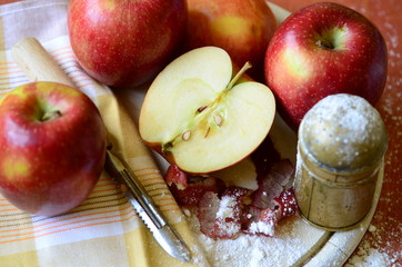 Sugar shaker andapples on wooden chopping board