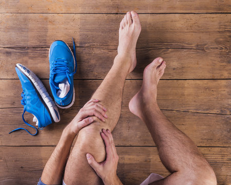 Unrecognizable injured runner sittin on wooden floor background