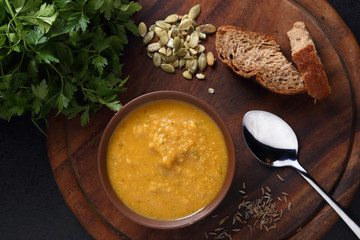 Pumpkin and lentil soup, bread and green on the wooden board