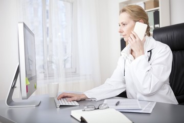 Female Doctor Calling Phone While Using Computer