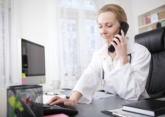 Female Doctor at her Office Dialing a Telephone - obrazy, fototapety, plakaty