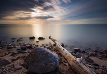 Rocky sea shore with driftwood at sunrise. Beautiful seascape