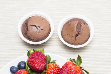Two chocolate cupcakes naer strawberries and blueberries