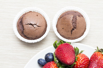 Two chocolate cupcakes naer strawberries and blueberries
