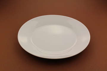 An empty white plate isolated on a brown background