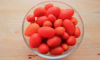 Place the tomatoes in a glass cup on a wooden floor.