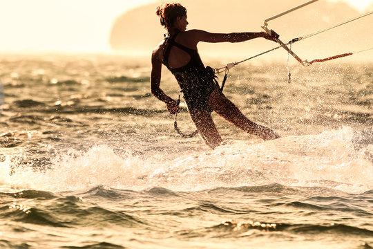 A young woman kite-surfer rides against the sun