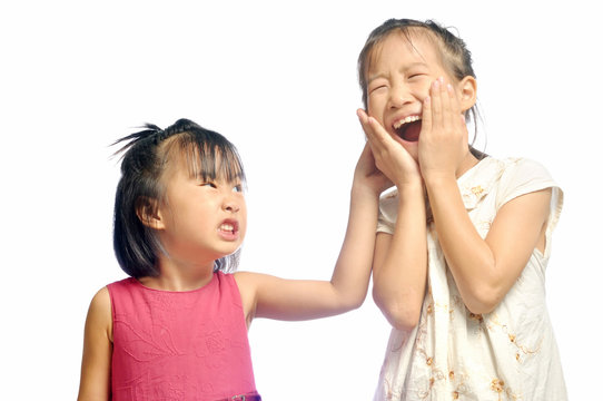 Siblings teasing, asian little girl pulling her sister's ear