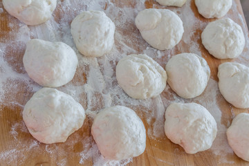Small balls of fresh homemade dough on floured wooden board