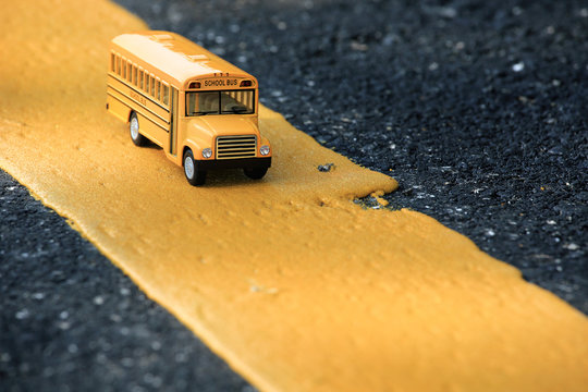Yellow school bus toy model on yellow line of country road.