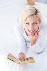 Smiling blonde woman lying on the bed and reading a book