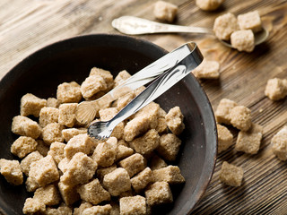 Cubes of cane sugar in the bowl on wooden table.