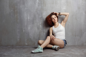 girl in a vest and sneakers sitting on a gray background texture
