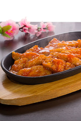 Sweet and sour chicken on a stone plate over wooden background
