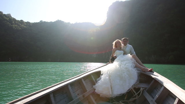 groom embraces bride sitting in longtail boat	
